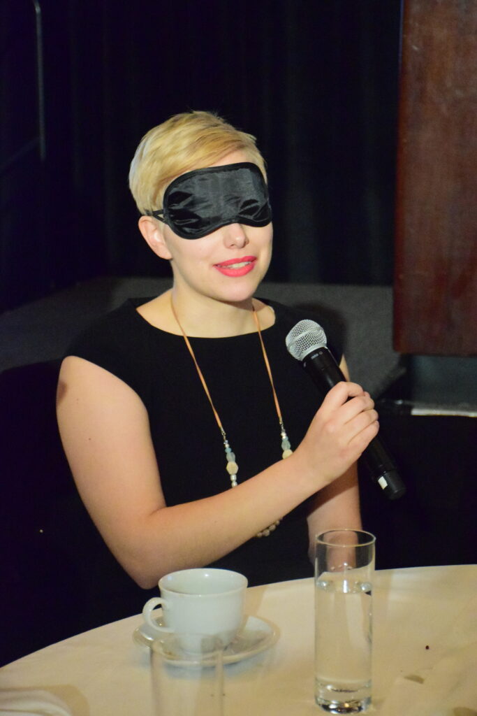 Women speaking at an in the dark event, wearing blindfold
